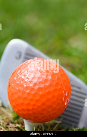 Frappant un coup de fer 3 sur une balle de golf orange tee en bois Banque D'Images