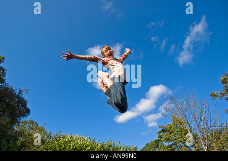 Portrait horizontal d'une jeune fille de race blanche au milieu de l'air contre un ciel bleu, de rebondir sur un trampoline. Banque D'Images