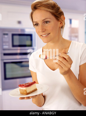 Femme dans la cuisine manger du gâteau au fromage Banque D'Images