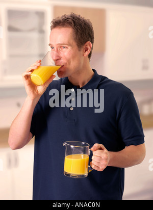 MAN IN KITCHEN DRINKING ORANGE JUICE Banque D'Images