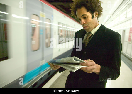 Commuter lit un papier de nouvelles sur une plate-forme de la gare Banque D'Images