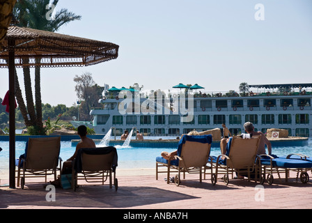 Movenpick Jolie Ville Luxor Hotel Île Crocodile assis au bord de la piscine en regardant passer les bateaux de croisière du Nil sur la rivière Banque D'Images