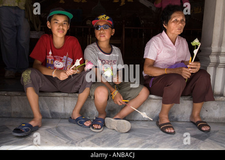 Adorateurs bouddhistes assis dans les cloîtres de Wat Phra Kaew, dans le complexe du Grand Palais, avec offrande de fleurs de lotus. Bangkok Thaïlande Banque D'Images