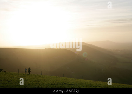 Un couple en train de marcher à travers la digue Devils près de Brighton dans la campagne anglaise comme le soleil se couche et le brouillard en rouleaux Banque D'Images