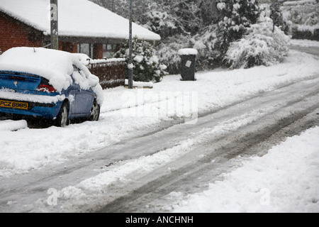 Les traces de pneus et les marques de voiture au milieu de la route de rue couverte de neige avec de la glace et de voiture en stationnement Banque D'Images