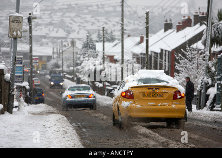 Les voitures qui circulent lentement le long de la route couverte de neige fondante de tourner les roues vers la petite ville Banque D'Images