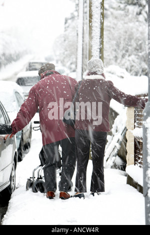 Personnes âgées infirmes couple en train de marcher le long sentier holding sur l'équilibre dans une tempête de neige Banque D'Images