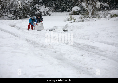 Deux enfants garçon et fille rouler en boule de grandes bien que la neige à côté des traces de pneus de voiture sur rue pour faire snowman Banque D'Images