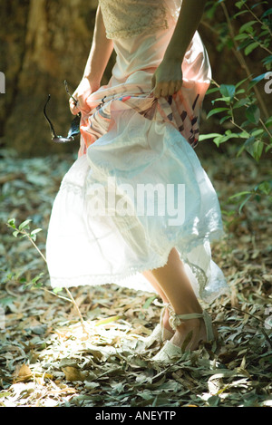 Young woman standing in woods, soulevant la jupe, taille en bas Banque D'Images