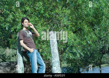 Casual man leaning against post, using cell phone Banque D'Images