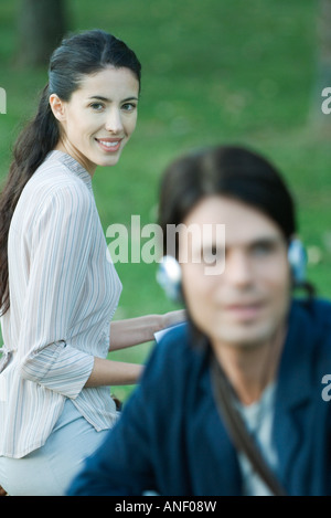 Les gens assis dans un parc, man listening to headphones, woman smiling at camera Banque D'Images