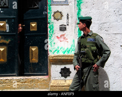 Une jeune fille palestinienne de piaulements à partir d'une porte et ressemble à un soldat israélien armé dans le quartier musulman de la vieille ville de Jérusalem-Est Israël Banque D'Images