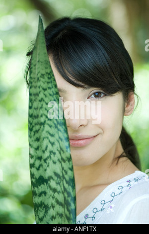 Woman holding up snake plant leaf en face de la moitié de la face, portrait Banque D'Images