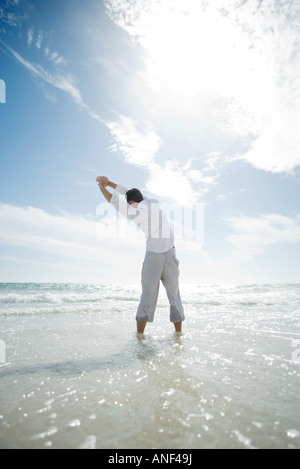 Jeune homme debout en surf, stretching Banque D'Images