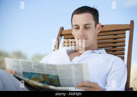 Young man reading newspaper in deckchair Banque D'Images