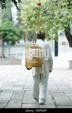 Un homme âgé dans les vêtements traditionnels chinois, portant cage à oiseaux sur l'arrière, vue arrière Banque D'Images