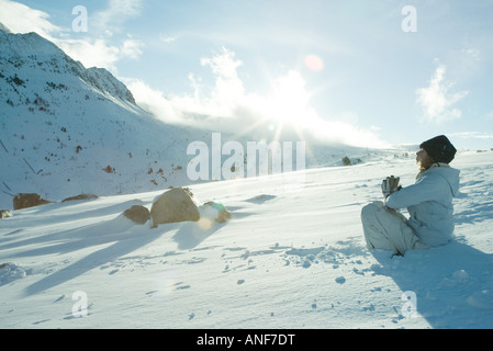 Teen girl sitting on snow en position de prière, soleil qui brille sur le bord de la mountain Banque D'Images