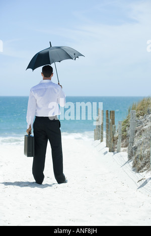 Woman under umbrella sur chemin de sable menant à l'océan, vue arrière Banque D'Images