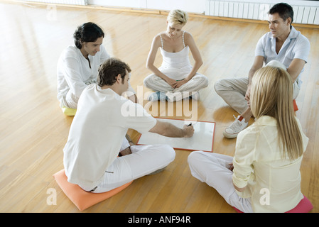 Groupe d'adultes assis sur des coussins sur le sol, un homme s'appuyant sur conseil chiffons pour effacement à sec Banque D'Images