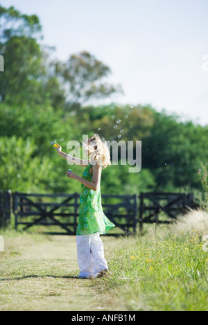 Woman blowing bubbles sur chemin rural, side view Banque D'Images