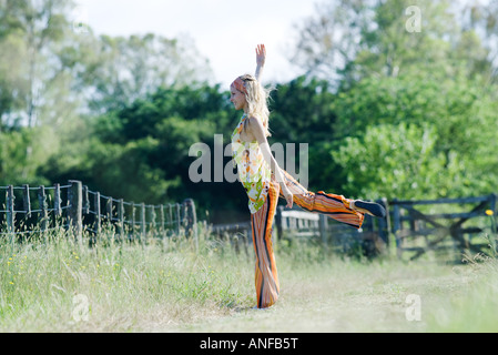 Jeune femme debout sur une jambe en domaine rural avec bras levé Banque D'Images