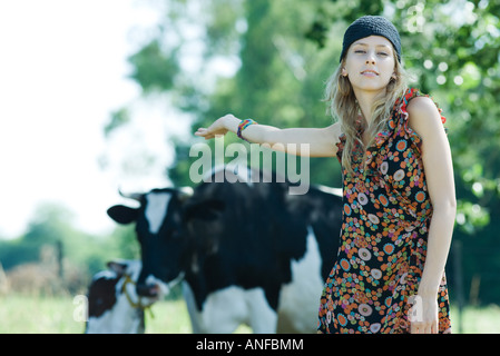 Jeune femme debout devant des vaches, bras tendus derrière elle, smiling at camera Banque D'Images