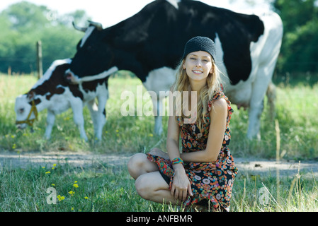 Jeune femme accroupie en face de vaches, smiling at camera Banque D'Images