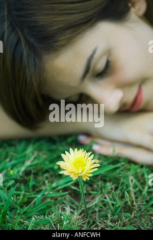 Young woman lying on grass avec tête posée sur les bras, les yeux fermés, de fleurs en premier plan, Portrait Banque D'Images