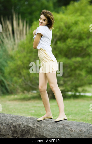 Young woman standing on log, smiling over Shoulder at camera Banque D'Images