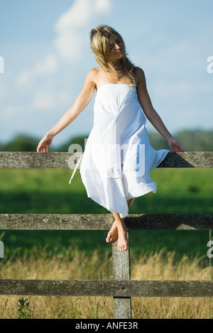 Young woman in dress sitting on rural clôture avec les bras, les yeux fermés Banque D'Images