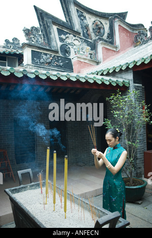 Jeune femme portant des vêtements traditionnels chinois, tenant l'encens dans cour du temple Banque D'Images