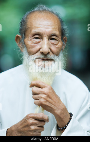 Homme âgé maintenant longue barbe blanche dans les mains, portrait Banque D'Images