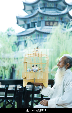 Un homme âgé portant des vêtements traditionnels chinois, holding up the birdcage, pagode en arrière-plan Banque D'Images