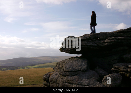Une jeune femme se dresse sur des rochers élevés à plus de Dartmoor, dans le Devon. Banque D'Images