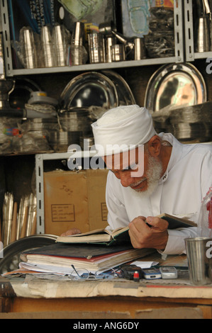 Un vieil homme portant un vêtement traditionnel égyptien de la lecture du Coran, livre sacré à la Smiths bazar dans la vieille ville du Caire Egypte Banque D'Images