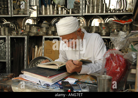 Un vieil homme portant un vêtement traditionnel égyptien de la lecture du Coran, livre sacré à la Smiths bazar dans la vieille ville du Caire Egypte Banque D'Images