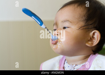 Baby Girl avec cuillère sortant de sa bouche. Banque D'Images