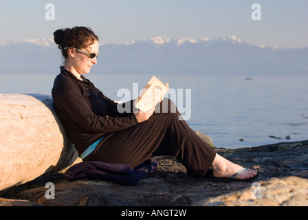 Une femme lisant un livre sur la plage, près de Victoria, Vancouver Island, British Columbia, Canada. Banque D'Images