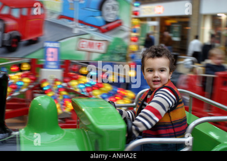 Petit garçon sur le rond-point passionnant et shoppers Noël ride afficher les fenêtres en arrière-plan Banque D'Images