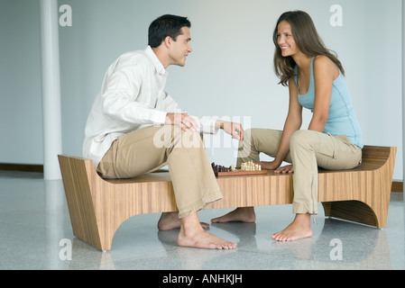 Jeune couple jouant aux échecs, smiling at each other Banque D'Images