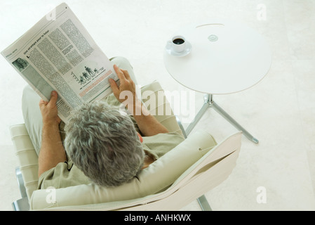 Homme assis, lisant le journal, high angle view Banque D'Images