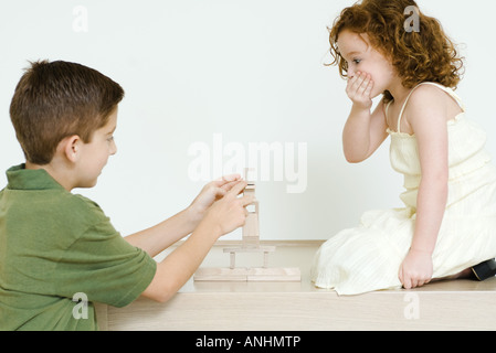 Boy stacking blocks alors que petite soeur montres, main sur la bouche Banque D'Images