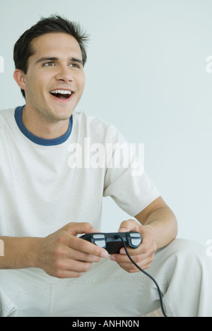 Jeune homme jouant des jeux vidéo, à la recherche du bâti, smiling Banque D'Images