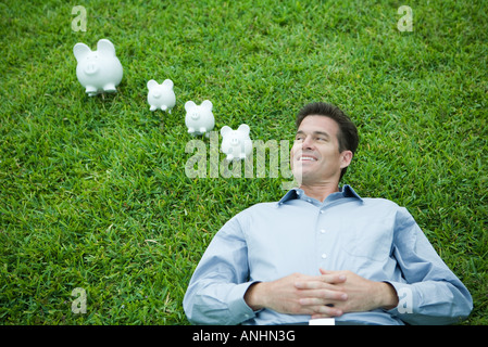 Homme étendu sur l'herbe, à côté de tirelires, smiling Banque D'Images