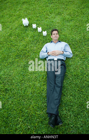 Homme étendu sur l'herbe, les yeux fermés, tirelire à côté de la tête Banque D'Images