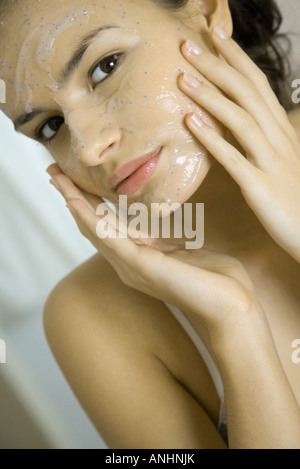 Young woman applying facial mask, looking at camera, portrait Banque D'Images