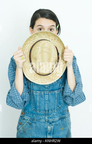 Teenage girl holding straw hat in front of face, looking at camera Banque D'Images