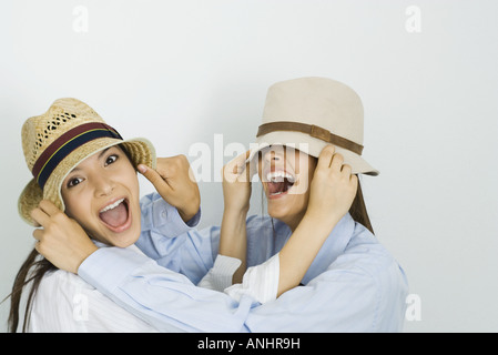 Deux jeunes amis chapeaux tirant sur les visages et souriant, un looking at camera Banque D'Images