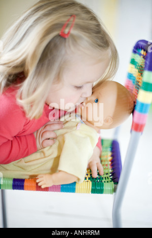 Blonde girl kissing baby doll Banque D'Images