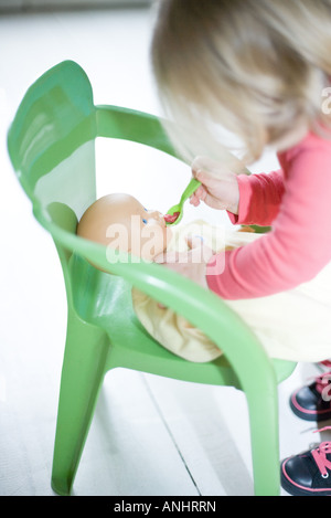 Blonde girl pretending to feed baby doll Banque D'Images